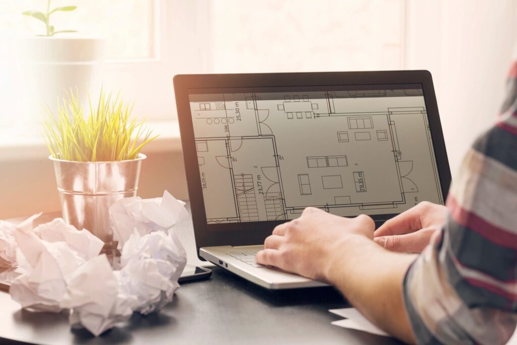 Closeup of female hands on a laptop with an architecture blueprint on the screen.